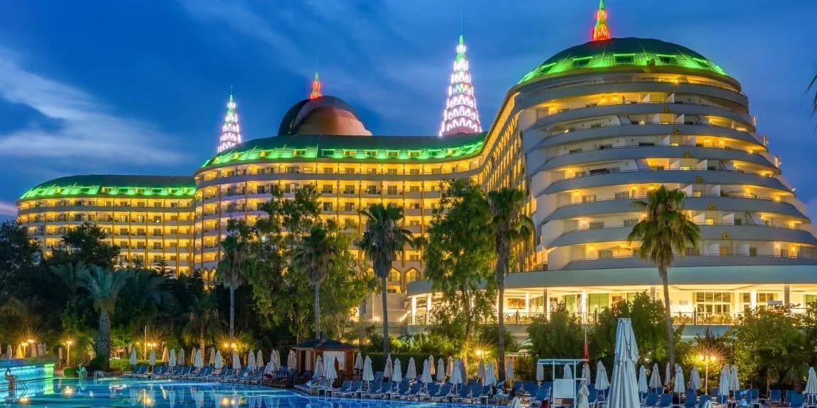 Oświetlone nocą budynki hotelu Delphin Imperial o zaokrąglonych, stopniowanych bryłach nad basenem