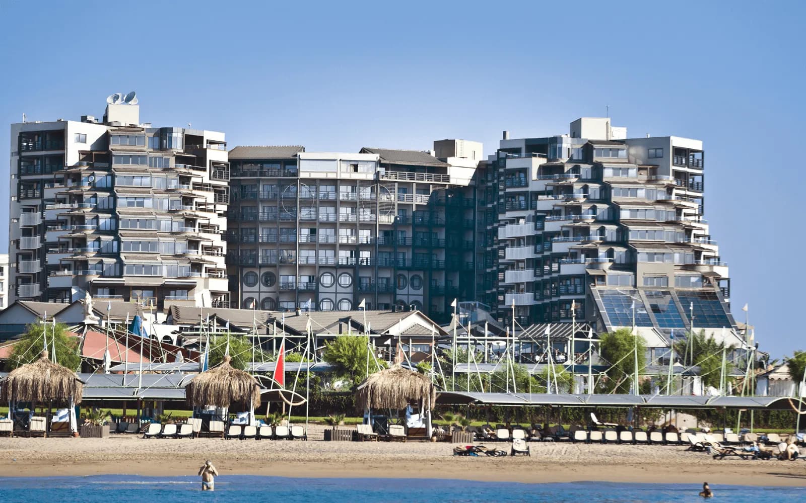 Tarasowe budynki hotelu Limak Lara De Luxe nad piaszczystą plażą z parasolami