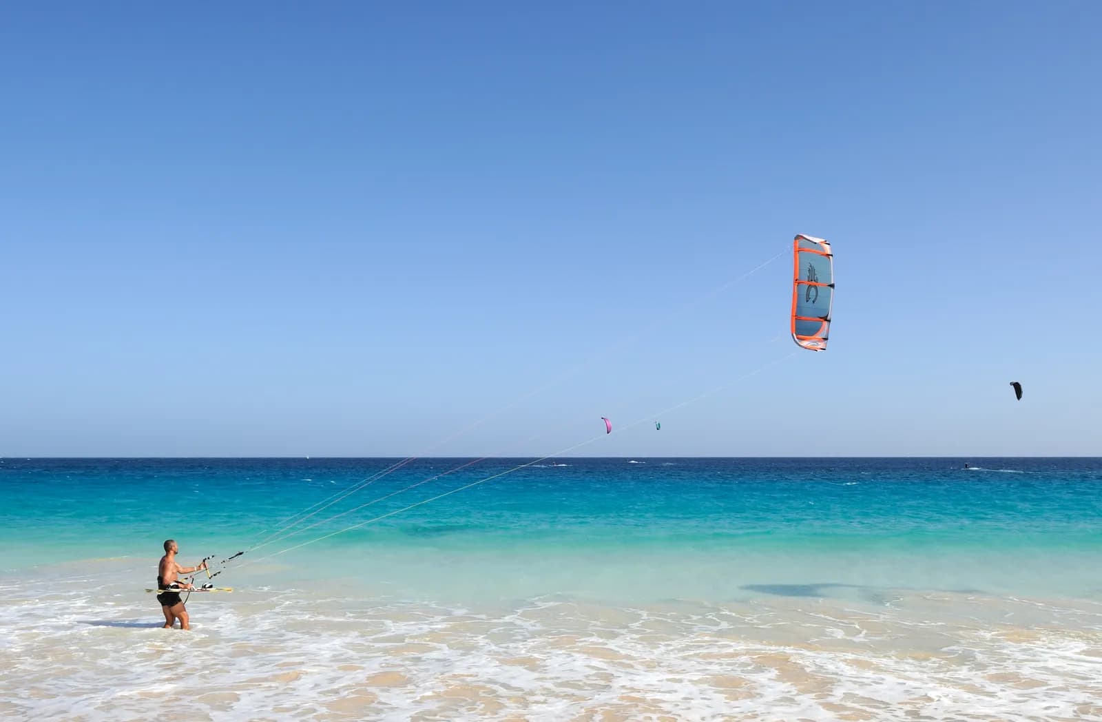 Kitesurfer z deską w płytkiej, turkusowej wodzie przy plaży na Sal, nad morzem kilka latawców